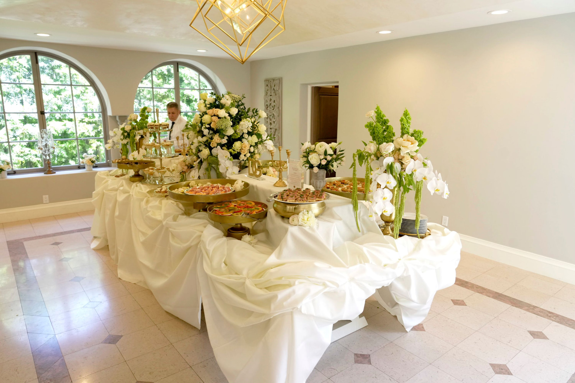 Catering table with florals and passed bites in an arched-window room